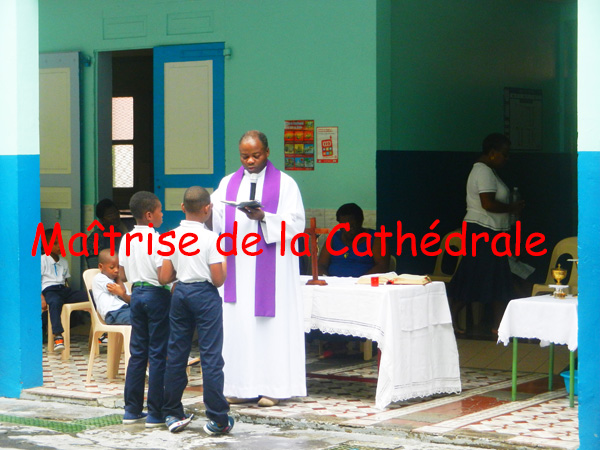 Le prêtre, avec écharpe violette, devant deux enfants