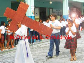 Quatre enfant marchent, le premier porte la croix de Jesus ainsi que l'habit de communiant
